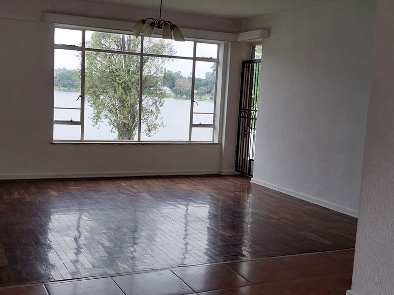 Spacious, empty living room featuring polished parquet flooring, large windows with scenic water views, and a secure entrance gate.