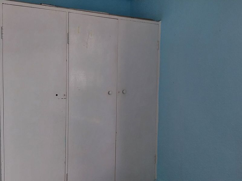 A bedroom featuring a built-in wardrobe and a window with exterior views. The room is vacant and requires cosmetic updates to improve its appeal.