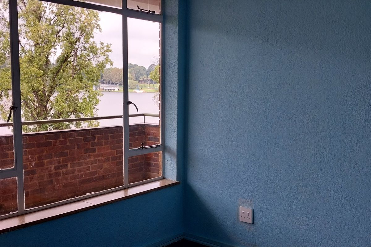 An empty bedroom featuring a large window with a view of the lake and balcony.