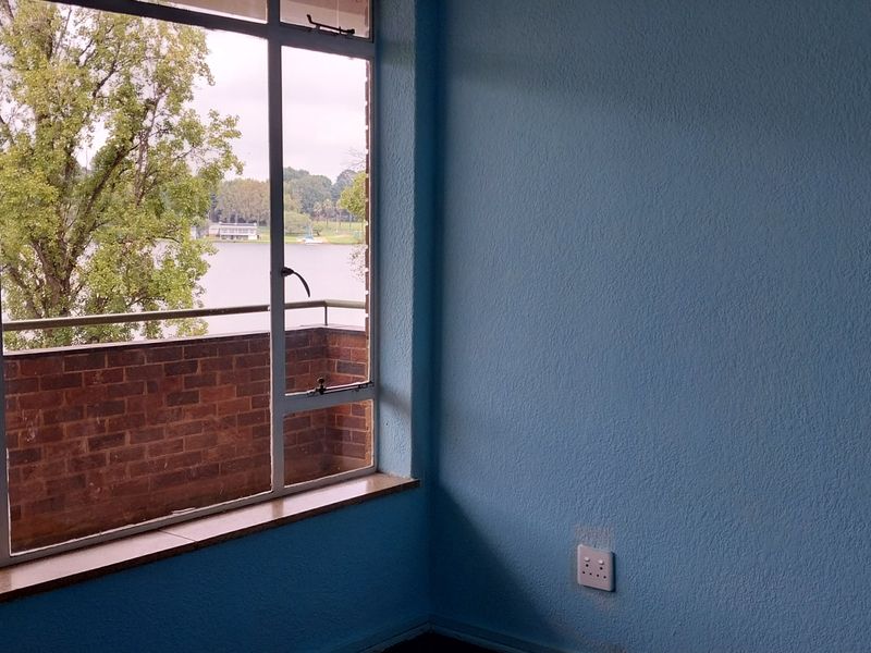 An empty bedroom featuring a large window with a view of the lake and balcony.