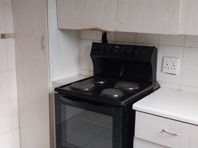 A dated kitchen area featuring built-in cabinetry, a freestanding electric stove, and tiled backsplash, showing signs of wear and finish damage.
