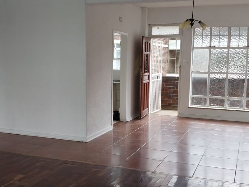 Spacious living area featuring a combination of parquet and tiled flooring, with direct access to an outdoor balcony through a secure timber door.