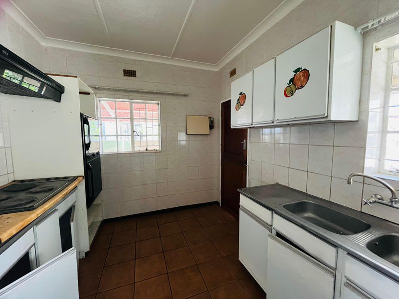 A functional, dated kitchen featuring tiled walls, built-in cabinetry, a stainless steel sink, and a hob with an extractor fan.