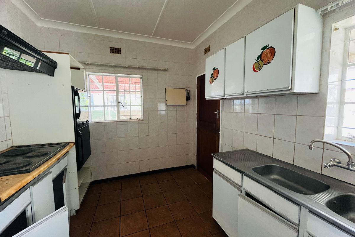 A functional, dated kitchen featuring tiled walls, built-in cabinetry, a stainless steel sink, and a hob with an extractor fan.