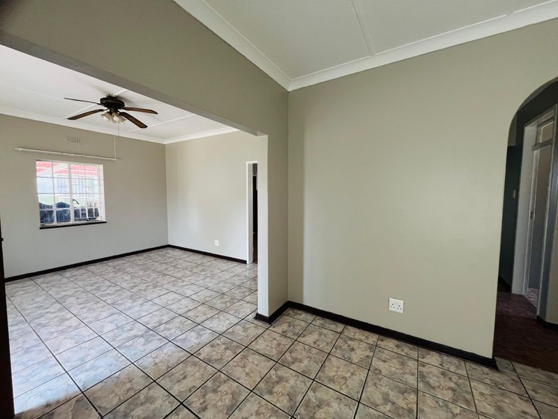An open-plan living area featuring neutral painted walls, ceramic tiled flooring, a ceiling fan, and an arched entryway leading to adjacent spaces.