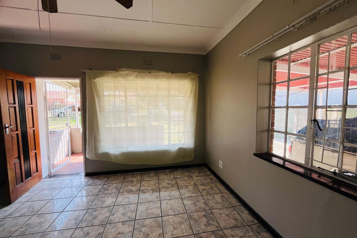 An empty living room featuring tiled flooring, a ceiling fan, and security features including burglar bars and a security gate.