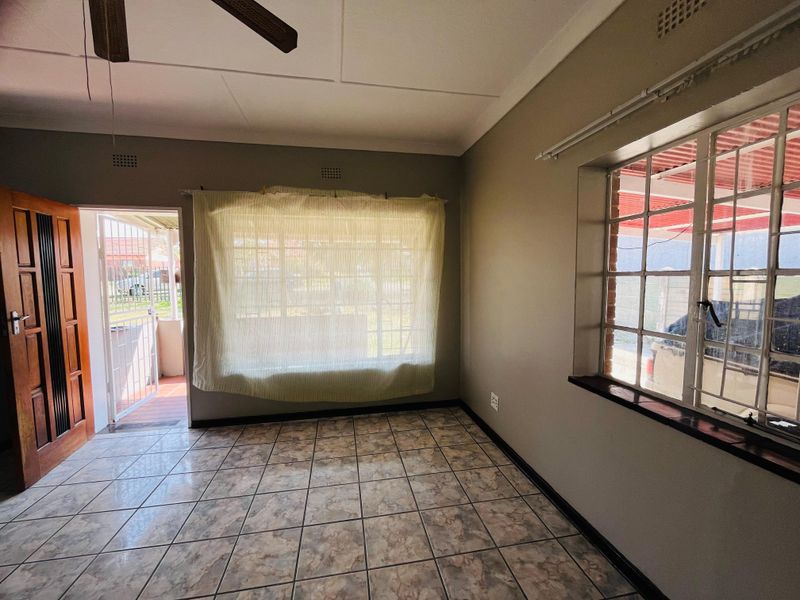 An empty living room featuring tiled flooring, a ceiling fan, and security features including burglar bars and a security gate.
