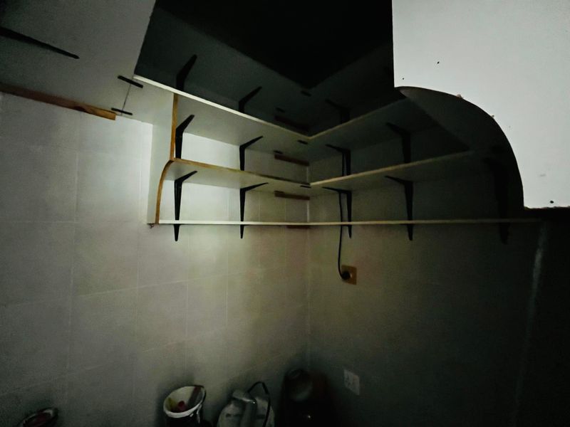 A small, dimly lit utility or scullery area featuring basic wall-mounted shelving and tiled wall finishes, requiring cosmetic updates.
