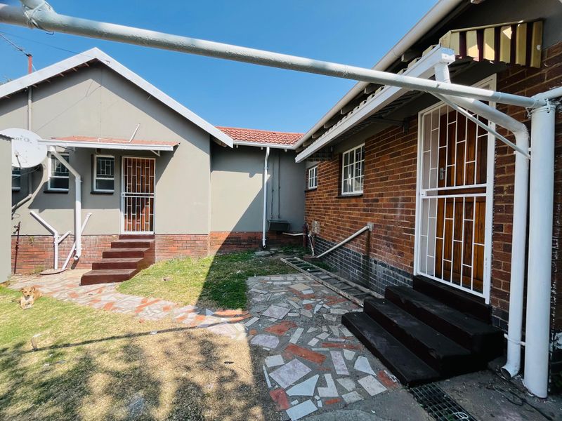 Rear exterior view of the house featuring a mix of brick and plastered finishes, security gates, and a paved courtyard area.