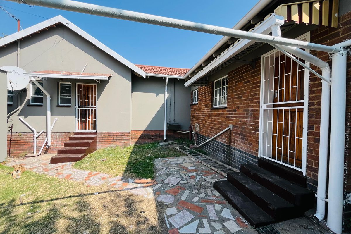 Rear exterior view of the house featuring a mix of brick and plastered finishes, security gates, and a paved courtyard area.