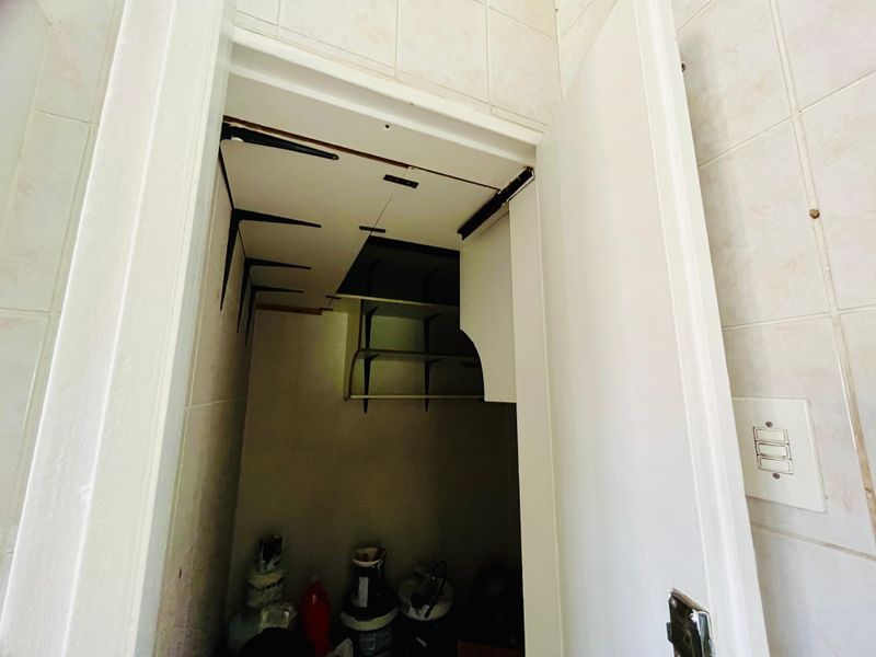 A small utility or storage closet featuring tiled walls and built-in shelving, currently showing signs of ceiling damage and wear.