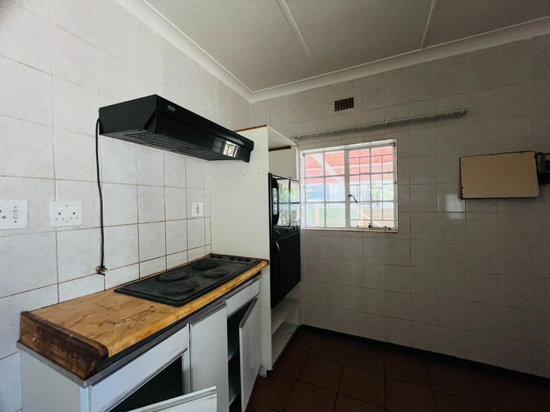 A functional kitchen space featuring tiled walls, a built-in oven, electric hob, and extractor fan, ready for modernization and cosmetic updates.