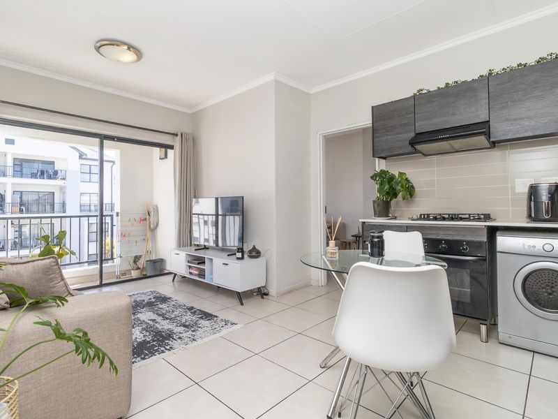 Open-plan living area featuring a modern kitchen with built-in cabinetry, gas hob, and tiled flooring, seamlessly connecting to a private balcony.