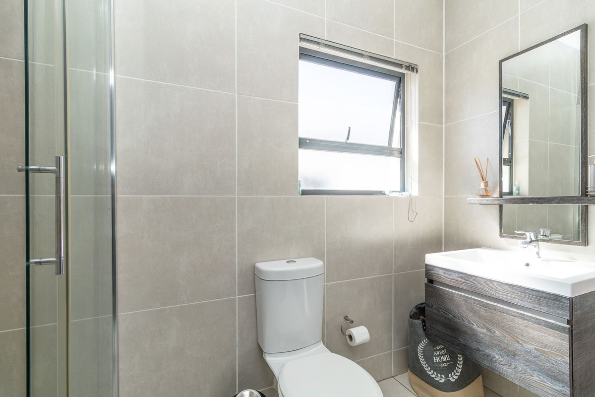 Modern bathroom featuring a glass shower enclosure, wall-mounted vanity with basin, and neutral floor-to-ceiling tiling.