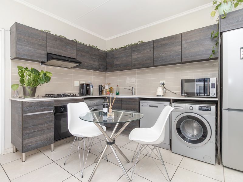 A modern, compact kitchen featuring dark wood-grain cabinetry, a gas hob, integrated appliances, and neutral tiled flooring, offering a functional and efficient cooking space.