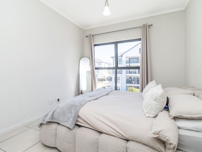 A bright and neutral bedroom featuring tiled flooring, large aluminium-framed windows, and simple coving detail, offering a clean and comfortable living space.
