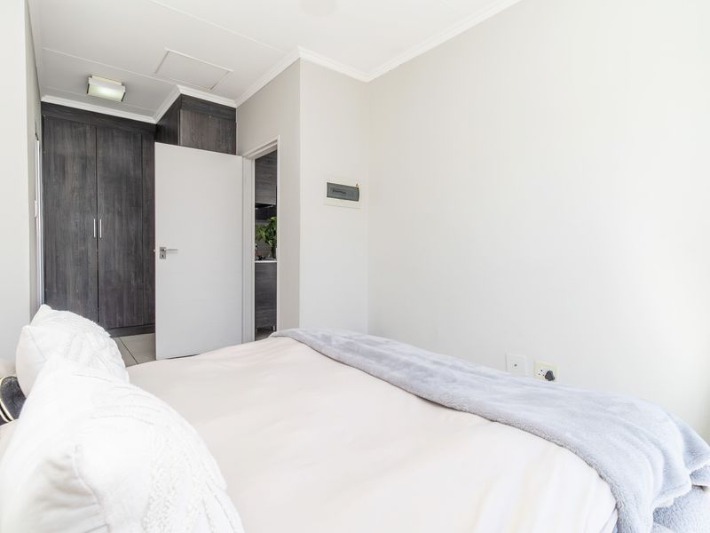 A well-maintained bedroom featuring built-in cupboards, neutral finishes, and tiled flooring, with direct access to an adjacent room.