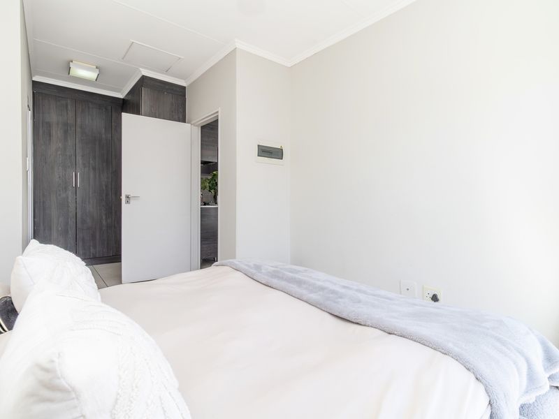 A well-maintained bedroom featuring built-in dark wood cupboards, neutral wall finishes, and access to an adjoining space.