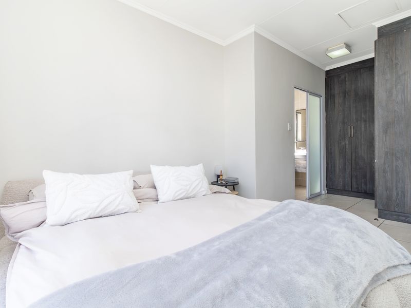 A well-maintained bedroom featuring built-in dark wood cupboards, neutral tiled flooring, and direct access to an en-suite bathroom.
