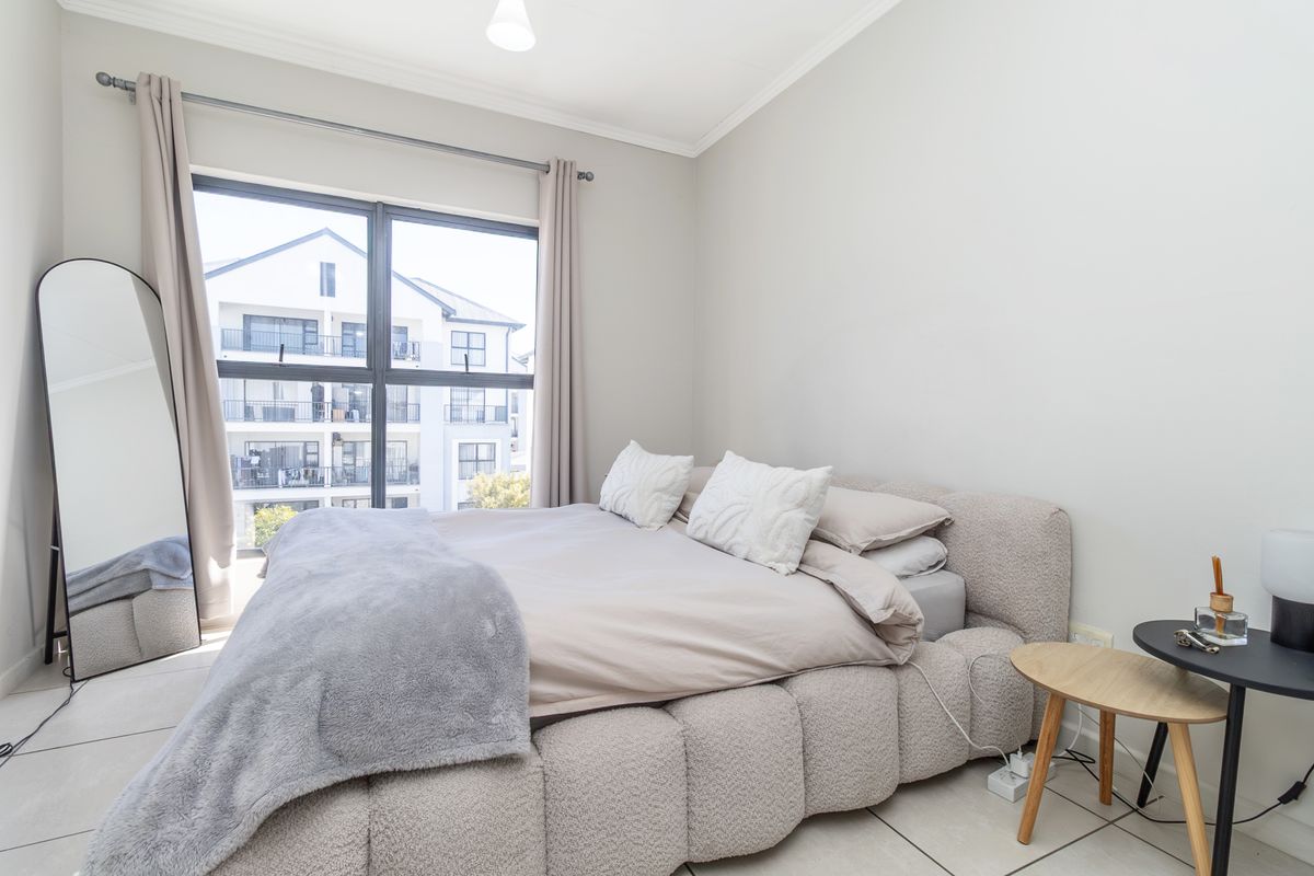 A bright and modern bedroom featuring large windows, neutral tiled flooring, and clean finishes, offering a comfortable and well-maintained living space.