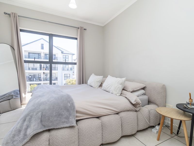 A bright and modern bedroom featuring large windows, neutral tiled flooring, and clean finishes, offering a comfortable and well-maintained living space.