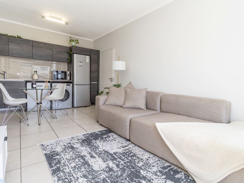 A modern open-plan living and kitchen area featuring dark wood cabinetry, tiled flooring, and a functional layout suitable for contemporary apartment living.