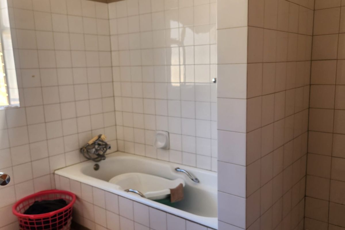 A dated bathroom featuring a built-in bathtub with white wall tiling and a separate shower area, requiring cosmetic updates to modernize the space.
