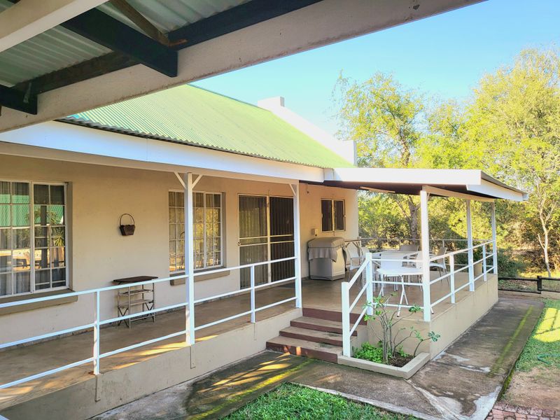 A covered outdoor patio area featuring a metal roof, white railings, and concrete flooring, providing direct access to the home through sliding glass doors.