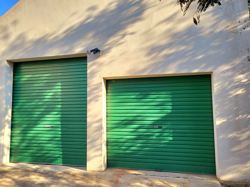 A double garage featuring green roller doors and exterior security lighting, set against a light-colored rendered facade.
