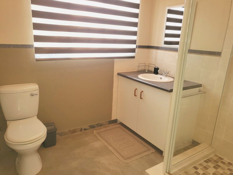 A functional bathroom featuring a vanity cabinet with a drop-in sink, a toilet, and a glass-enclosed shower with tiled finishes.