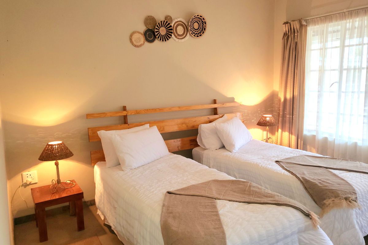 A cozy bedroom featuring twin beds, neutral wall tones, and natural light filtering through window curtains.
