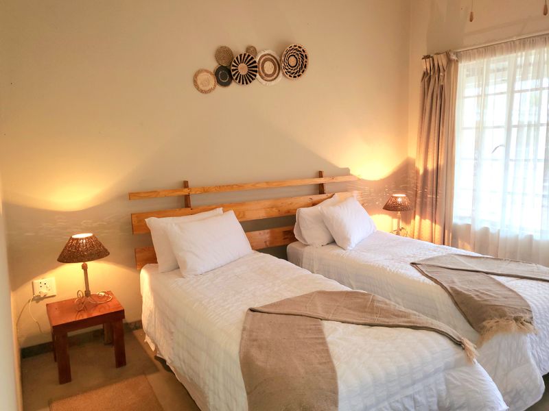 A cozy bedroom featuring twin beds, neutral wall tones, and natural light filtering through window curtains.