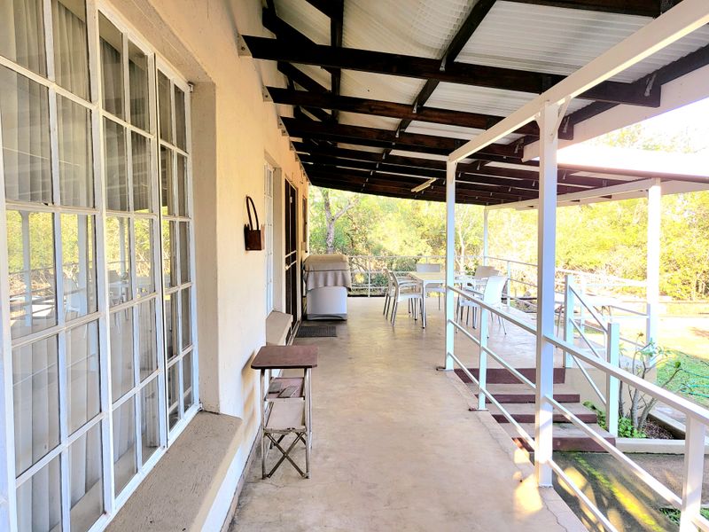 A spacious covered patio featuring exposed timber rafters, concrete flooring, and metal railings, offering a functional outdoor entertainment area overlooking the garden.