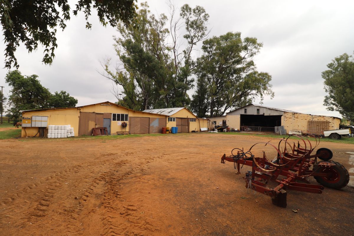 A wide view of farm outbuildings and storage sheds situated on a large dirt yard, featuring corrugated metal structures and open-bay storage areas.