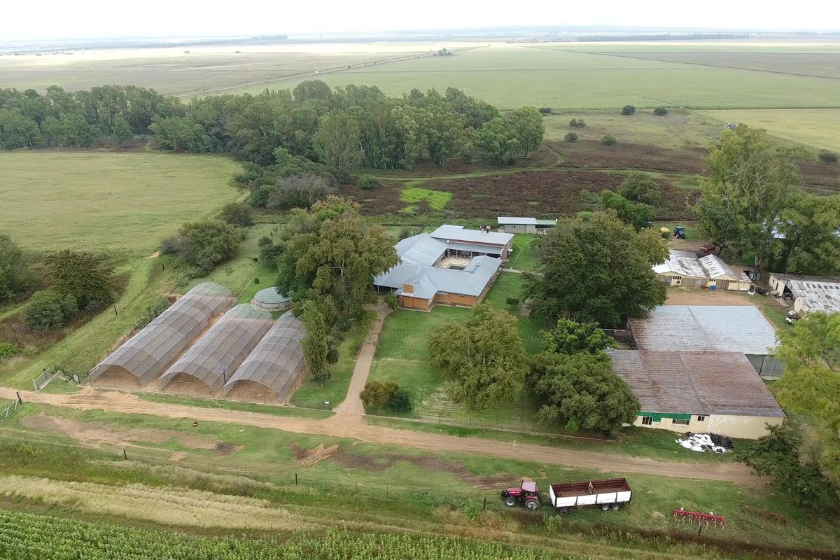 Aerial view of a farm property featuring a central main dwelling, multiple agricultural outbuildings, greenhouse structures, and surrounding open farmland.