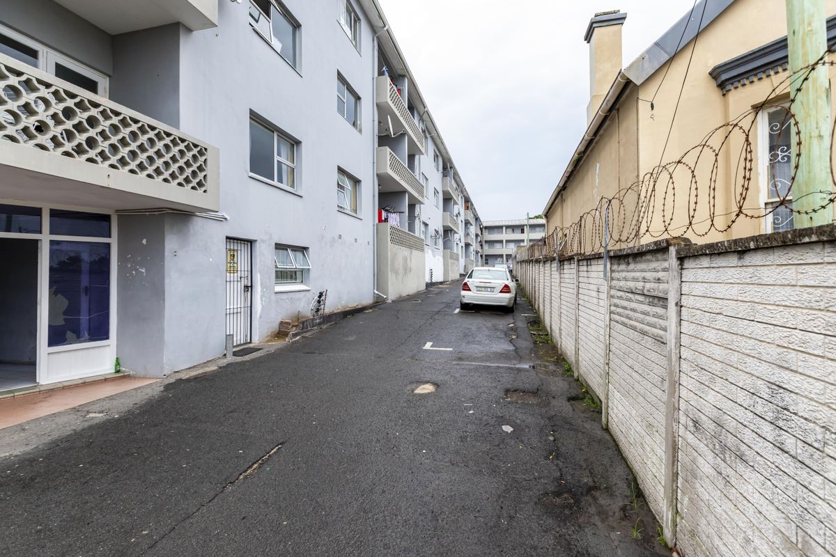 Exterior view of the apartment building complex showing the driveway, access points, and perimeter boundary wall with security fencing.