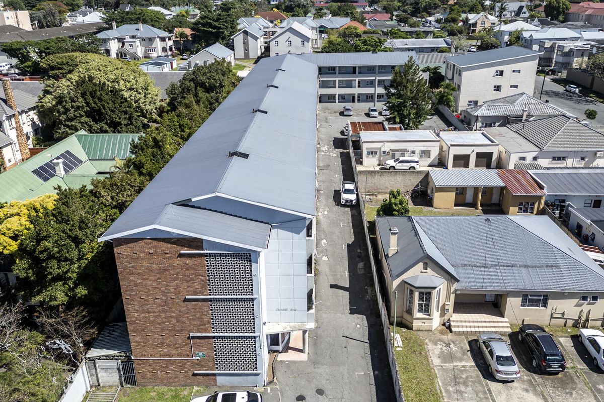 Aerial view of a multi-story apartment building featuring a metal roof, brick facade, and an adjacent paved driveway area within a residential neighborhood.