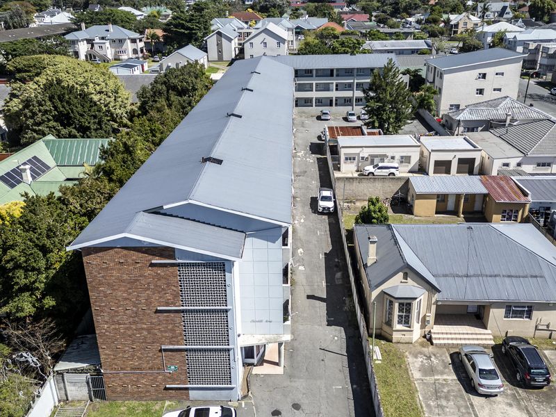 Aerial view of a multi-story apartment building featuring a metal roof, brick facade, and an adjacent paved driveway area within a residential neighborhood.
