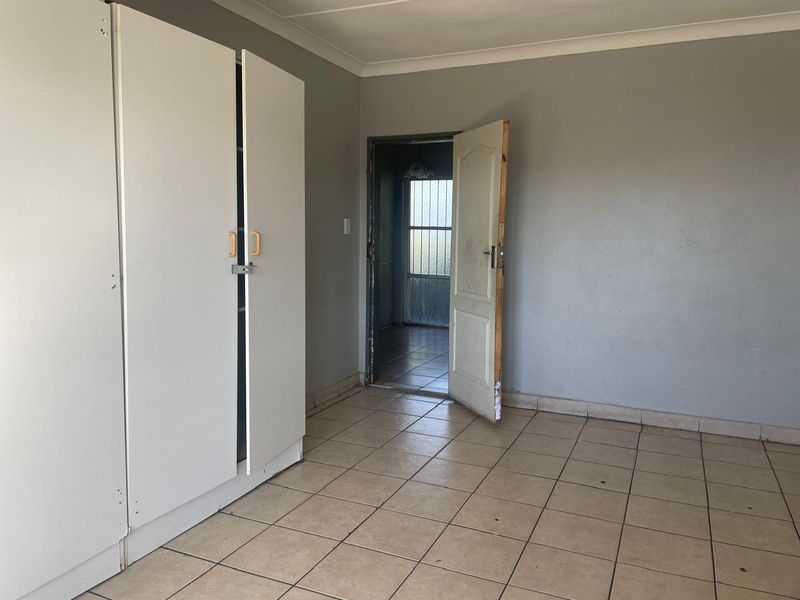 A bedroom featuring built-in cupboards, tiled flooring, and a doorway leading to an adjacent space.