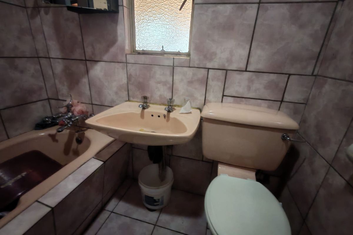 A dated bathroom featuring original peach-toned sanitaryware, fully tiled walls and flooring, and an obscured glass window for privacy.