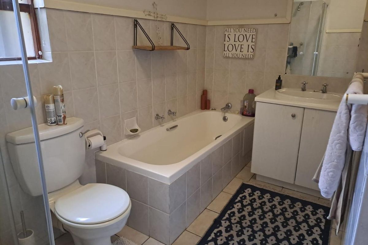 A functional bathroom featuring a built-in bathtub, vanity cabinet with integrated sink, and a toilet, finished with neutral wall tiling.