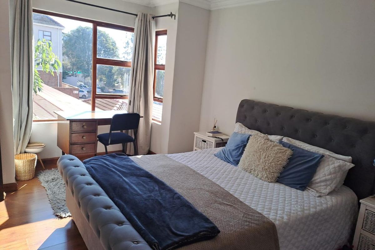 A bright bedroom featuring large windows with natural light, wooden flooring, and crown molding, offering a comfortable and well-maintained living space.