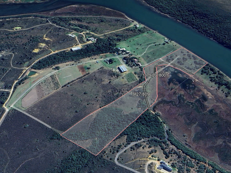 Aerial view of a large vacant residential plot featuring natural landscape, river frontage, and clear boundary demarcations.