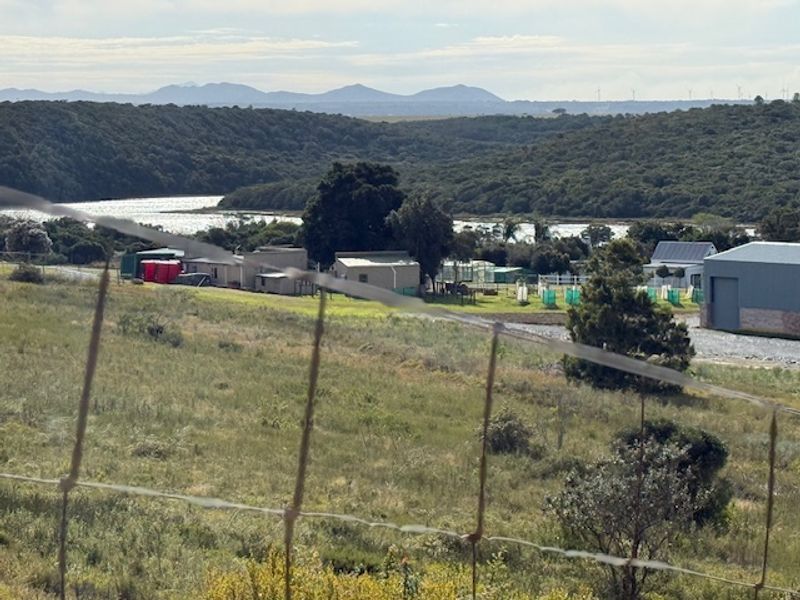 A scenic view overlooking a rural landscape with distant hills, water, and existing structures, captured from behind a wire fence.
