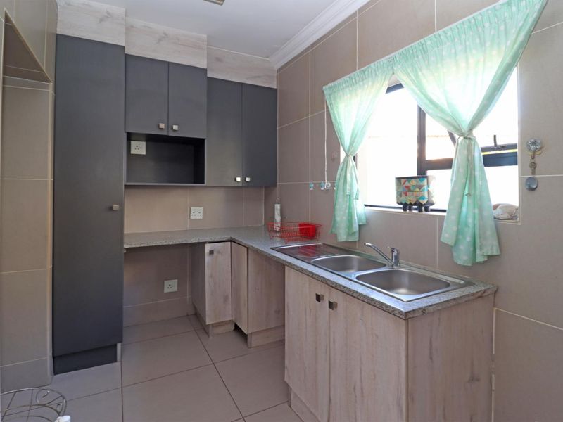 A clean and functional kitchen featuring modern grey and wood-grain cabinetry, granite countertops, and a double bowl stainless steel sink.