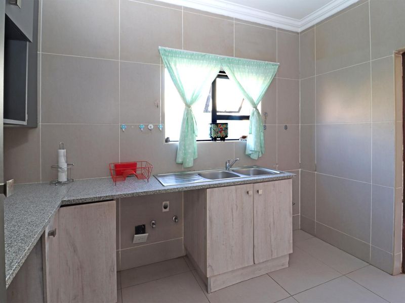 A functional scullery area featuring tiled walls, granite countertops, and a double stainless steel sink with built-in cabinetry and plumbing connections.