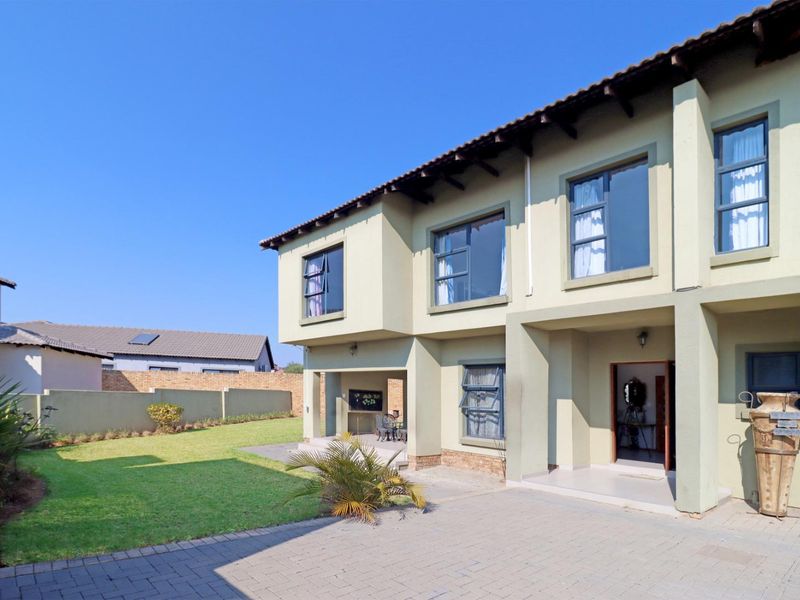 Rear view of a two-story house featuring a paved driveway, a covered patio with a built-in braai, and a well-maintained garden.