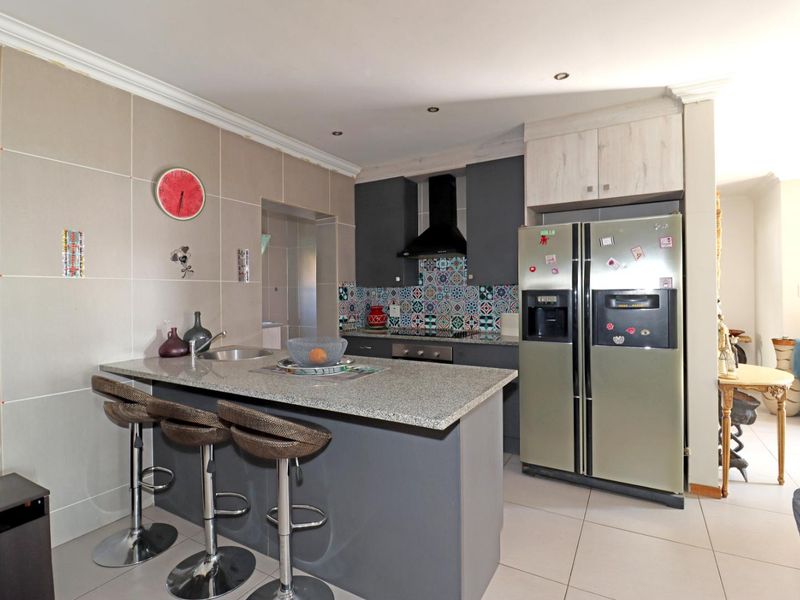 Modern kitchen featuring a central island with granite countertops, patterned tile backsplash, built-in oven, extractor fan, and sleek cabinetry.