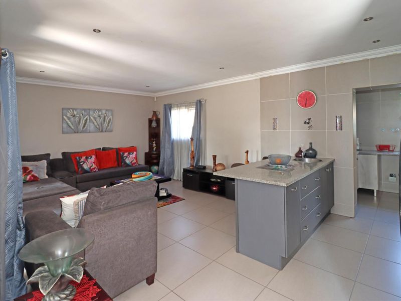 Open-plan living area featuring a central kitchen island with granite countertops, tiled flooring, and recessed lighting, seamlessly connecting to the lounge space.
