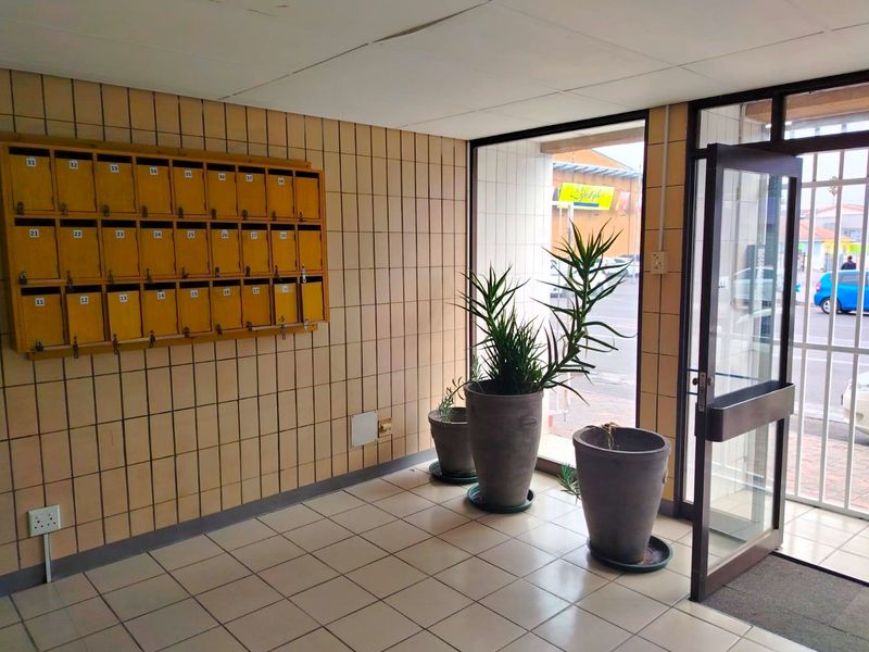Apartment building entrance lobby featuring tiled flooring, wall-mounted mailboxes, and a glass security door leading to the exterior.